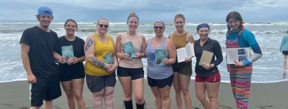 Students and staff who traveled abroad to Costa Rica pose for a photo on the beach with the book, My Life with Sea Turtles.