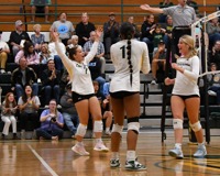 Three Centurion volleyball platers celebrate together on the court.