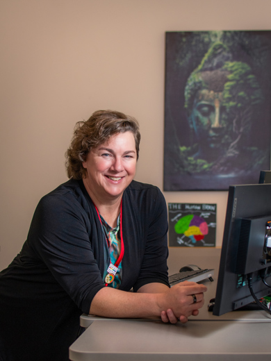 Instructor Jessica Snyder leaning on a classroom teaching station and wearing a gray cardigan.
