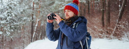 Young man with beard and knit hat outside in snow taking pictures