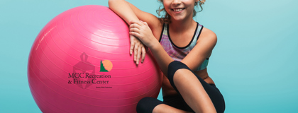 Little girl in leotard sitting next to large pink rubber ball.