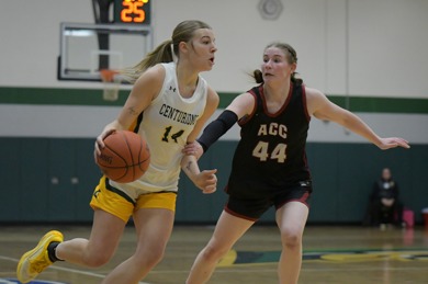MCC women's basketball player dribbling the ball on the court while an opposing team member attempts to steal the ball. Her uniform number is 14.