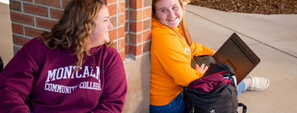 Female students sitting outdoors near brick wall