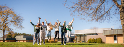 Six students outside on MCC's Sidney campus jumping in the air excitedly.