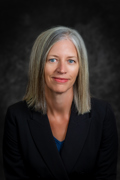 Headshot of Theresa Rowland wearing a blakc blazer with a blue shirt underneath. She has gray/blonde hair and blue eyes.