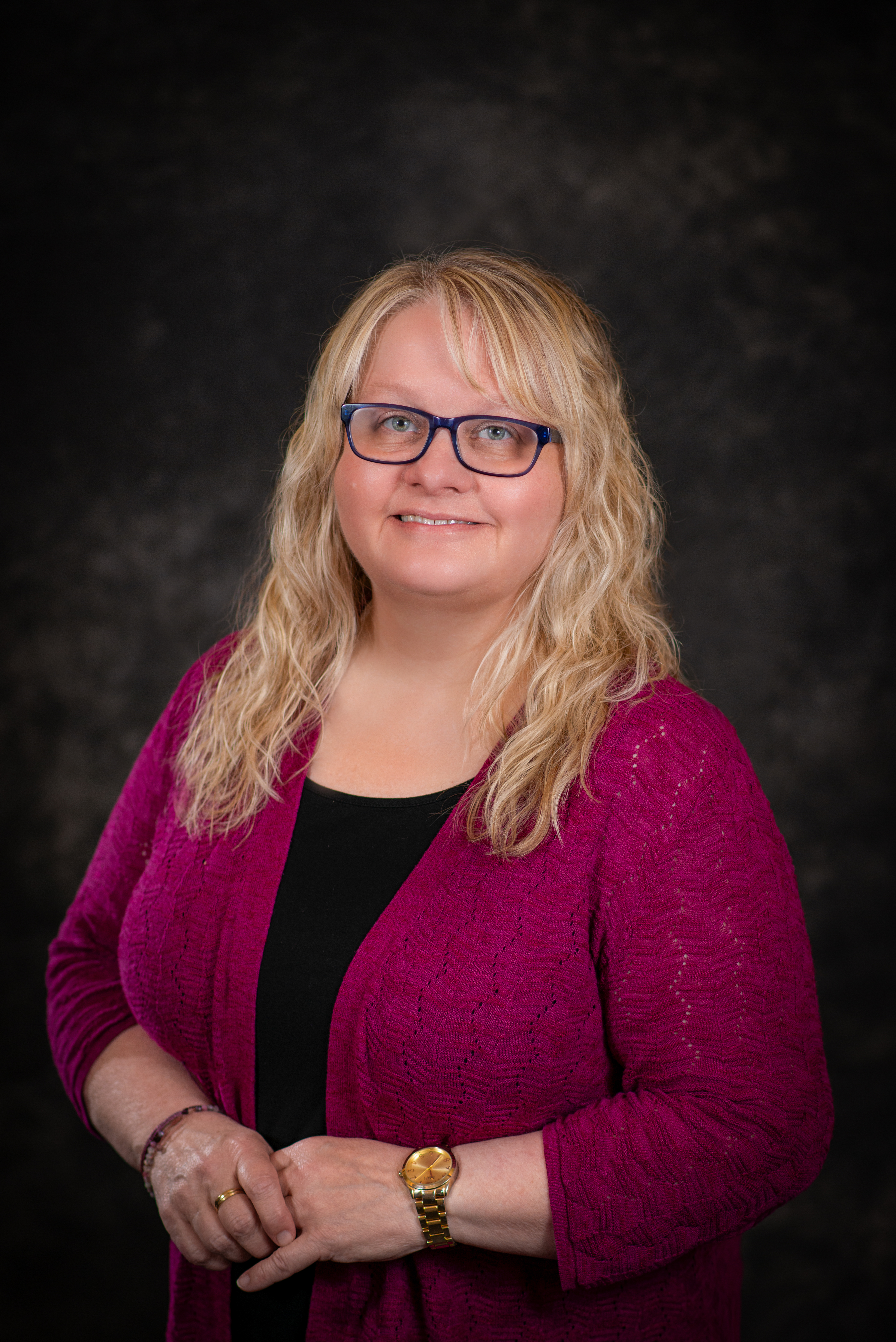 Professional photo of Marlo Tiffany weraing a fuschia cardigan with hands clasped and smiling at the camrera.