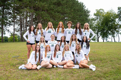 Team shot of the women's volleyball team for the 26-27 season. They are outside sitting on green grass with trees in the background.