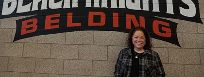 Belding High School Counselor Jodi Edwards in front of brick wall with high school logo on it. 