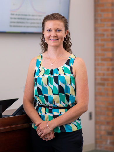 Instructor Katey Johnson standing in a classroom wearing a black, blue and yellow patterned top.