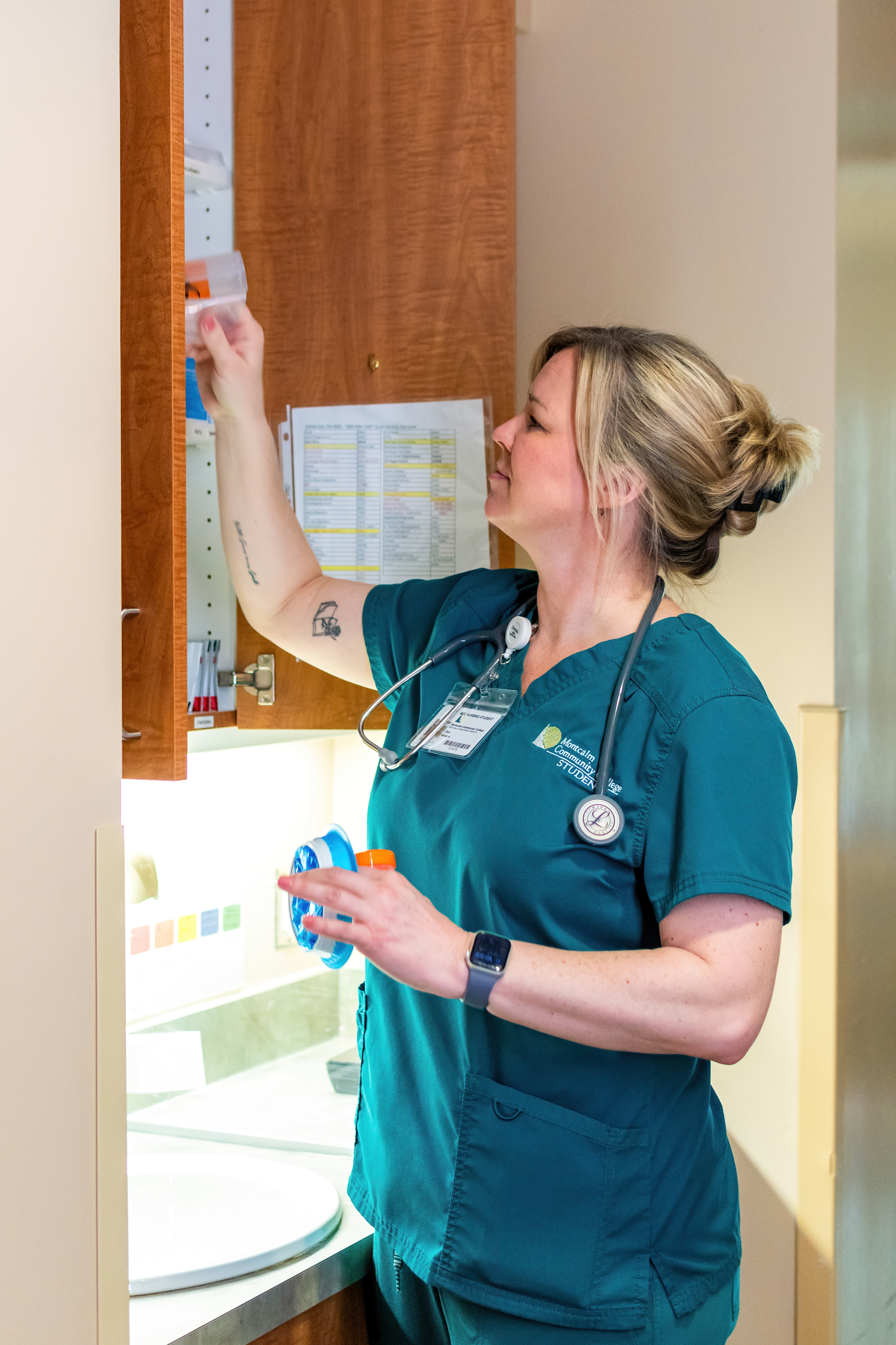 MCC nursing student in green scrubs pulling supplies out of a cabinet at a clinical partner location.