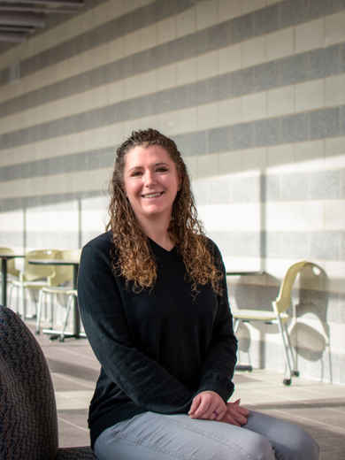 Instructor Brianne Lodholtz sitting on a chair and smiling at the camera. She is wearing a black top and gray pants. 