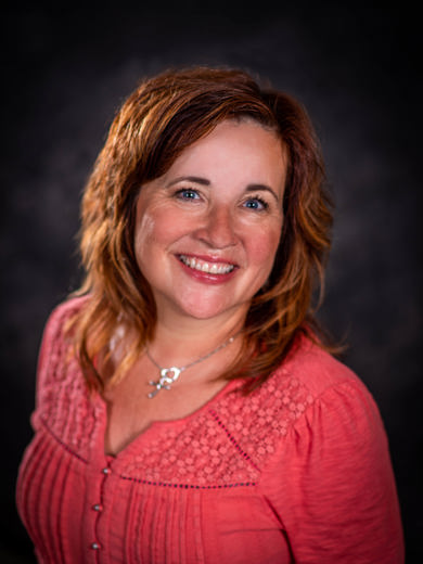 Headshot of Amy Denslow wearing a coral pink shirt and a silver necklace.