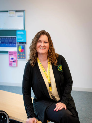 Instructor and Career Advisor Amy Zdanowski sitting on a desk wearing a black cardigan and yellow shirt smiling at the camera. 