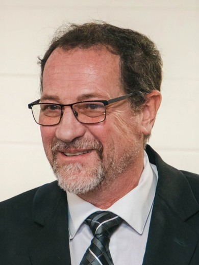 Headshot of Scott Smith wearing a black suit with a blue, black and white plaid tie.