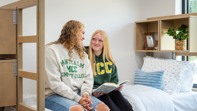 Two MCC students sitting on a bed in Carbonelli Villas studying together.