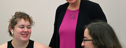 An MCC faculty member stands between two students who are sitting and having a conversation.