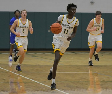 Three MCC men's basketball players running down the court during a game. Number 11 is dribbling the ball and is flanked by number 5 and number 23.