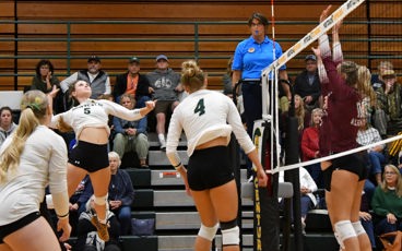 Montcalm Community College volleyball player spikes the ball during a match as opponents prepare to block at the net.