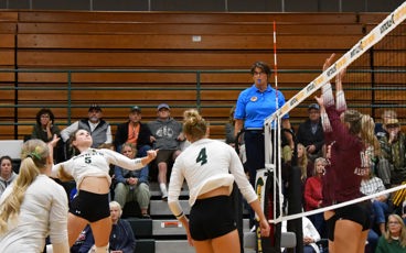 Montcalm Community College volleyball player spikes the ball during a match as opponents prepare to block at the net.