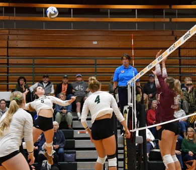Montcalm Community College volleyball player spikes the ball during a match as opponents prepare to block at the net.