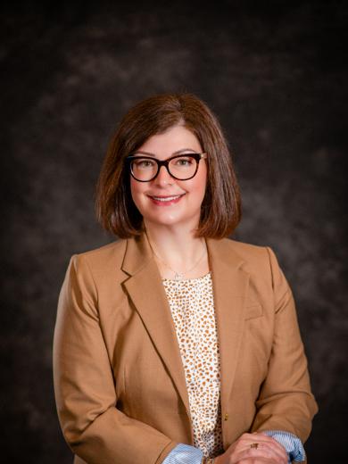 Headshot of instructor Erin Busch-Grabmeyer wearing a tan blazer with a patterned shirt underneath.
