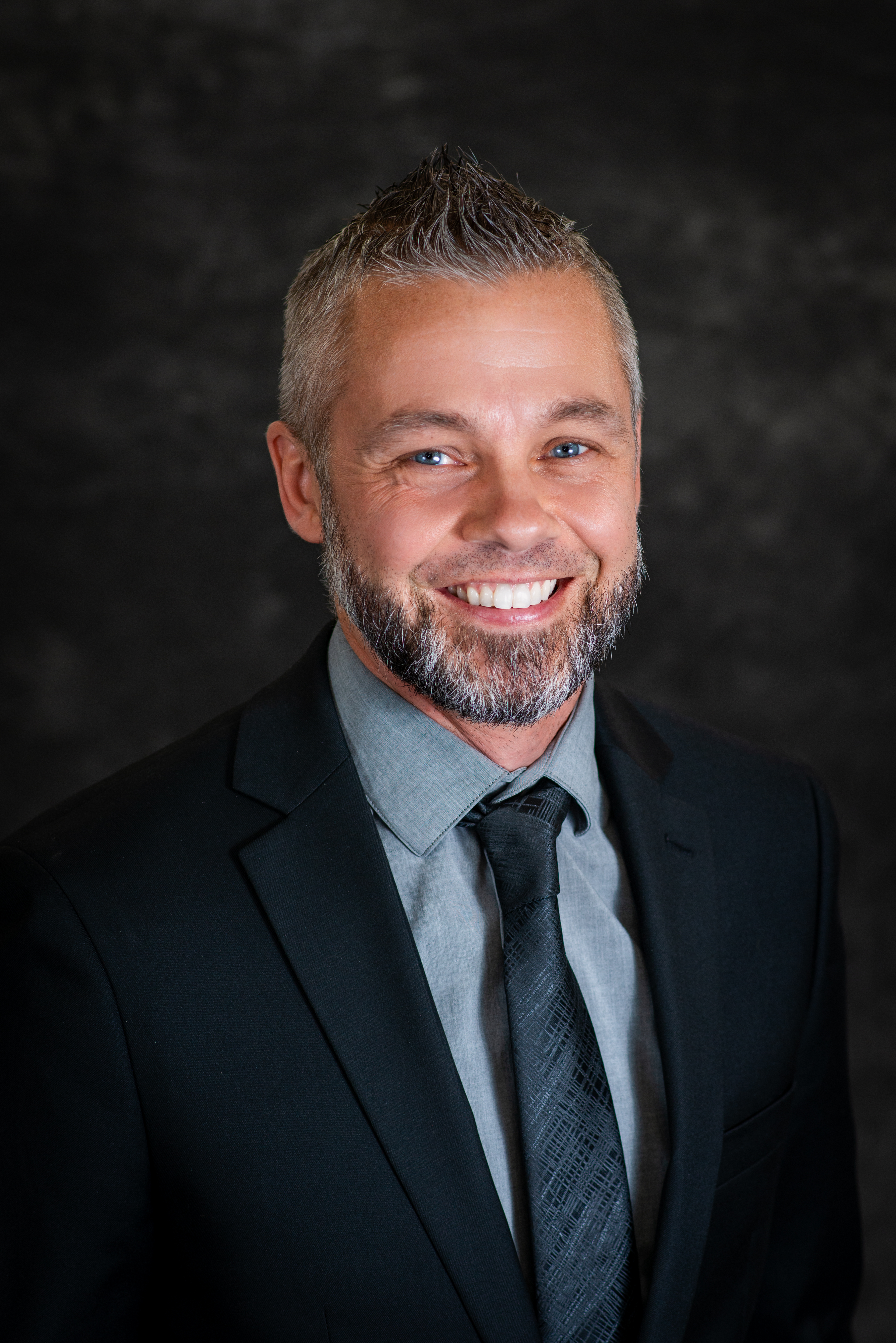 Headshot of Robert Byram wearing a black suit jacket, gray shirt and black tie.