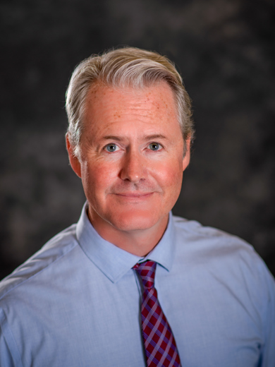 Headshot of instructor Ben Stancil wearing a light blue shirt with a red plaid tie.