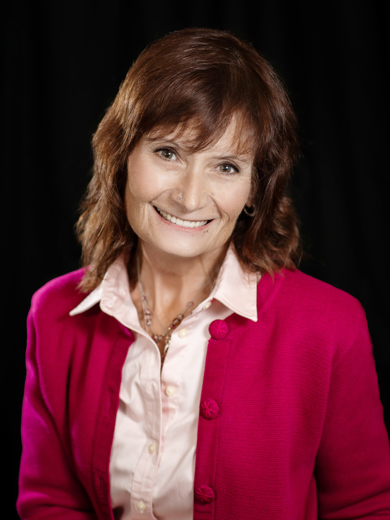 Headshot of Elana Powell wearing a hot pink cardigan over a baby pink button down shirt and a beaded necklace.