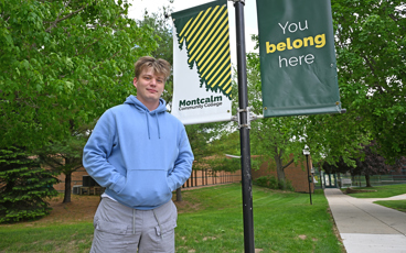 Tyler Williams standing outside of and MCC building near a sign that reads "You belon here"