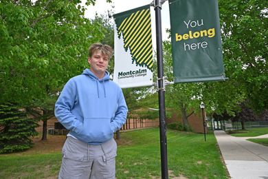 Tyler Williams standing outside of and MCC building near a sign that reads "You belon here"