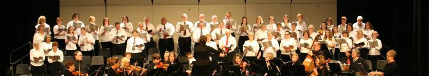 A large orchestra, choir and the conductor are photographed performing on a stage.