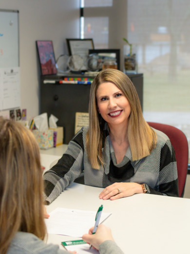 Instructor and Counselor Brand Baldwin Bunting smiles at the camera while hleping a student in her office.