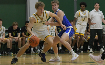 MCC men's basketball player dribbling the ball on the court during a game. An oppossing player attemps to boxout. He is wearing uniform number 5.