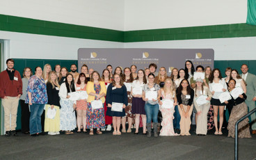 Scholarship recipients stand with faculty, staff, and supporters in front of a Montcalm Community College Foundation backdrop while holding award certificates.