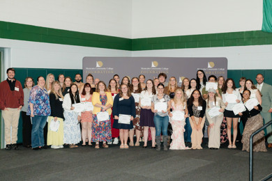 Scholarship recipients stand with faculty, staff, and supporters in front of a Montcalm Community College Foundation backdrop while holding award certificates.
