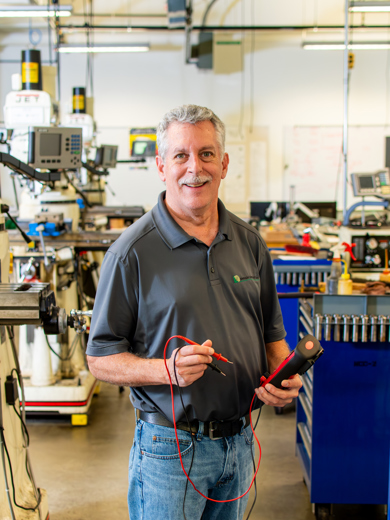 Instructor Jeff Pedelty standing in an instruction room wearing a gray MCC polo with jeans and smiling at the camera.